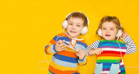the happy laughing two children with headphones look in the camera on a yellow background with copy space/