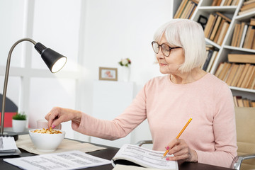Healthy snack. Appealing mature woman consuming snack while writing