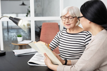 Repeat after me. Ambitious tutor carrying book while senior woman reading