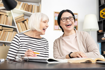 Remember words. Merry tutor carrying book while senior woman laughing