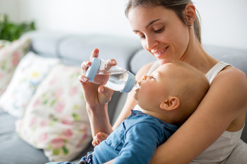Mother, feeding her baby boy from bottle, sitting on the couch at home