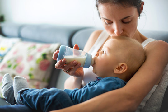 Mother, feeding her baby boy from bottle, sitting on the couch at home