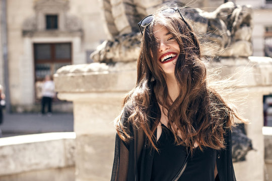 happy stylish woman with gorgeous smile and hair, having fun in sunlight in city street. beautiful hipster girl in fashionable outfit, waving hair and smiling. luxury look. carefree and happiness