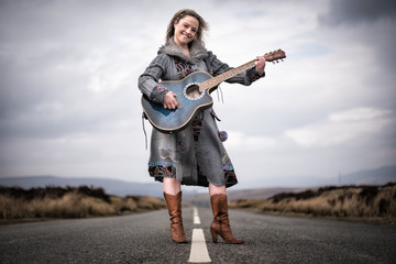 Obraz premium Young happy woman standing in middle of a road and playing guitar