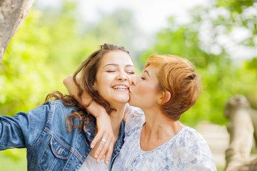Fototapeta premium Mother and daughter hug each other, happy and smiling, summer out in the park 