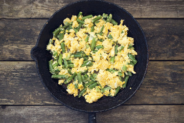 Green beans fried with eggs beautiful in an old frying pan on a wooden background, rustic style