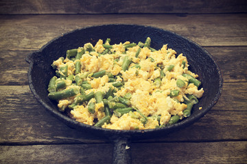 Green beans fried with eggs beautiful in an old frying pan on a wooden background, rustic style