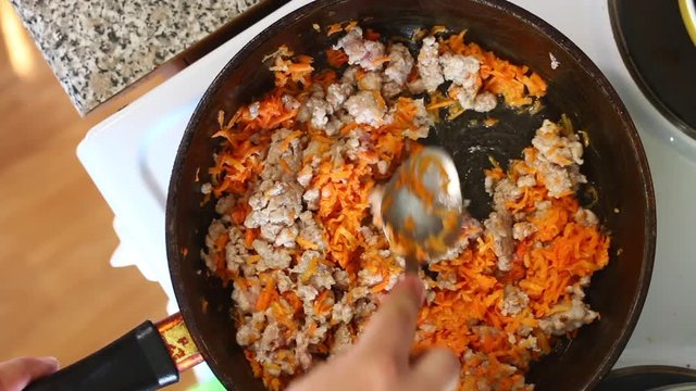The man mixes stuffing and chopped carrots in a frying pan