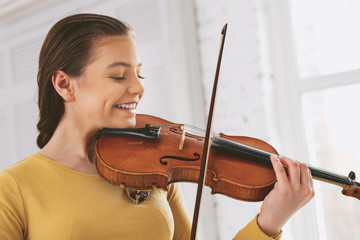 Positive thoughts. Cheerful brunette holding violin near neck while playing classical music