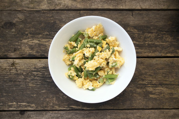Green beans fried with eggs beautiful in a plate on a wooden background, rustic style