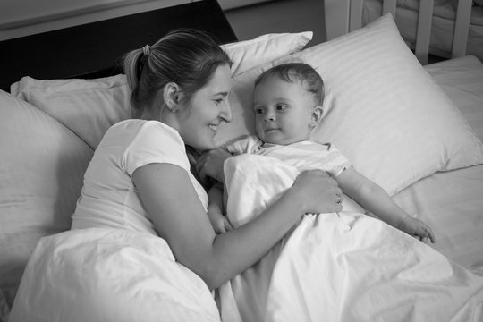 Portrait of smiling baby boy looking at happy mother lying with him in bed