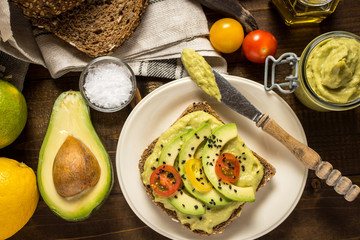 Fresh Avocado Spread Guacamole and Slices with Cherry Tomato and Black Sesame on a Piece of Bread. Healthy Breakfast Concept.