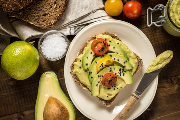 Fresh Avocado Spread Guacamole and Slices with Cherry Tomato and Black Sesame on a Piece of Bread. Healthy Breakfast Concept.