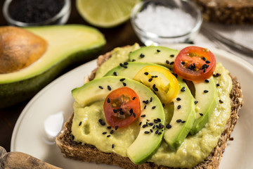 Fresh Avocado Spread Guacamole and Slices with Cherry Tomato and Black Sesame on a Piece of Bread. Healthy Breakfast Concept.