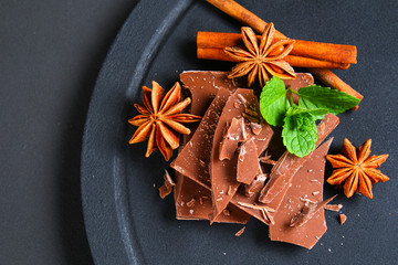 Pieces of chocolate, cinnamon and star anise on a dark grey table.