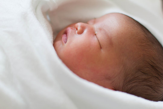 Newborn infant baby girl in white blanket sleeping in bed