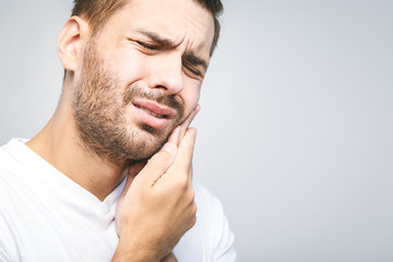 Toothache. Handsome young man suffering from toothache, closeup, touching his cheek to stop pain against white background. Strong toothache