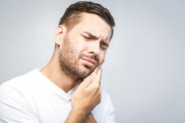 Fototapeta premium Toothache. Handsome young man suffering from toothache, closeup, touching his cheek to stop pain against white background. Strong toothache