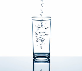 Fresh drinking water dropping into glass with bubbles on white background