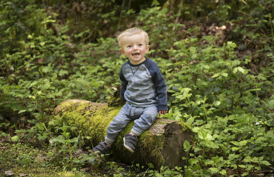 Two year old boy sitting on a log in a green park 