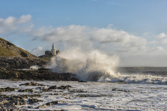 Landscape image of Mumbles lighthouse with waves crashing against the rocks 
