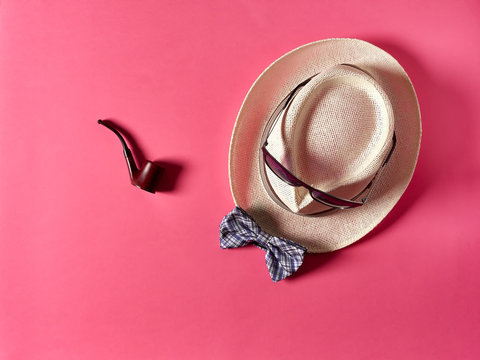 Nice Smoking Pipe Lying On Pink Background Near Straw Hat With Sunglasses And Bow Tie