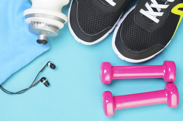Pink dumbbells, sport bottle, headphones and running shoes on the sport mat