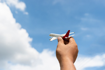 Man's hand holding a toy plane against the blue sky with clouds..