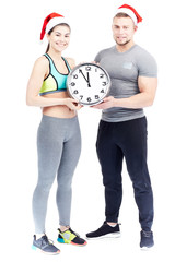 Portrait of athletic young man and woman wearing Santa hats and holding clock