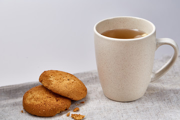White porcelain mug of tea and sweet cookies on homespun napkin over white background, top view, selective focus