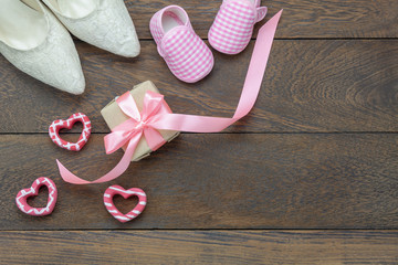 Table top view aerial image of decoration Happy Mothers day holiday or fashion clothing background concept.Flat lay gift box & shoes women and kids with heart on modern brown wooden plank with space.
