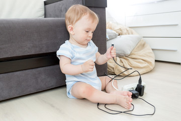 Unattended little boy playing with electric socket and cables at home