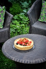 In a green garden in the nature fruit pie with strawberries and other berries. On a woven table