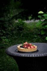In a green garden in the nature fruit pie with strawberries and other berries. On a woven table