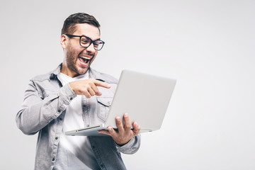 Funny young handsome man in shirt holding laptop and smiling while standing against white background. Have fun.