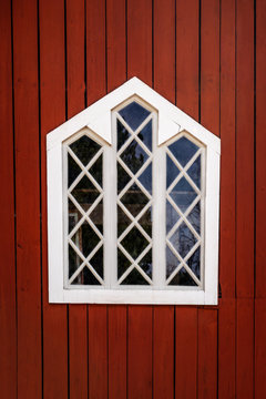 One white decorative traditional window with wooden frame on a red barn wall.