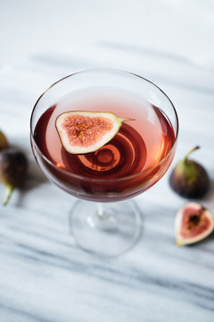 Summer cocktail aperitif with figs on a marble table.