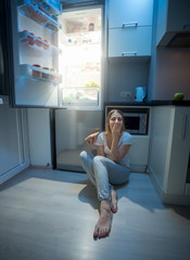 Fototapeta na wymiar Sleepy hungry woman sitting on kitchen floor at night and holding pizza