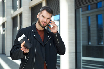 An attractive man with a beard and short hair alarmingly and irritably looks into the camera talking on the phone. 