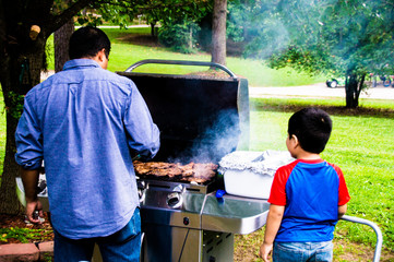 Latino dad cooking on a grill outside while son watches