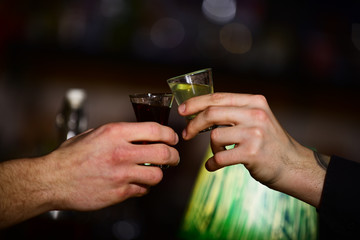 Male hands cheers with alcohol on blurred bar background.
