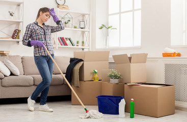 Young tired woman cleaning new home with mop
