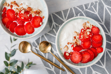 Top view on two bowls with coconut yoghurt, fresh strawberries and almonds. The concept of breakfast and a healthy lifestyle. Scandinavian style.
