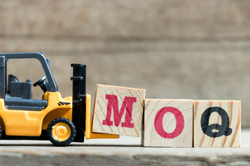 Toy yellow forklift hold letter block M to complete word MOQ (Abbreviation of Minimum Order...