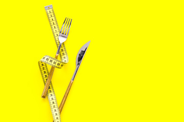 Diet, weight loss, slimming concept. Fork and knife with wound measuring tape on yellow background...