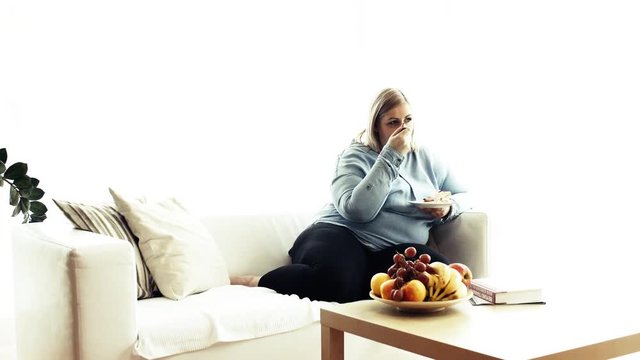 An attractive overweight woman at home, eating cake.