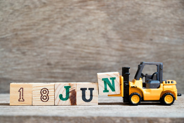 Toy forklift hold block N to complete word 18 jun on wood background (Concept for calendar date in month June)