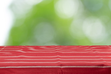 An empty table with a red striped tablecloth and an green natural background in the morning in the garden. For your food and product display montage.