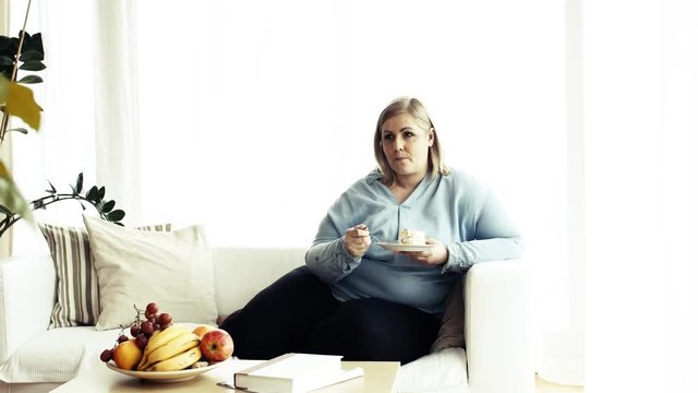 An attractive overweight woman at home, eating cake.