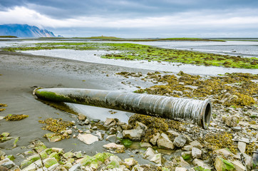 An abandoned broken pipe comes out of the black volcanic sand on the deserted Hofn beach in Iceland